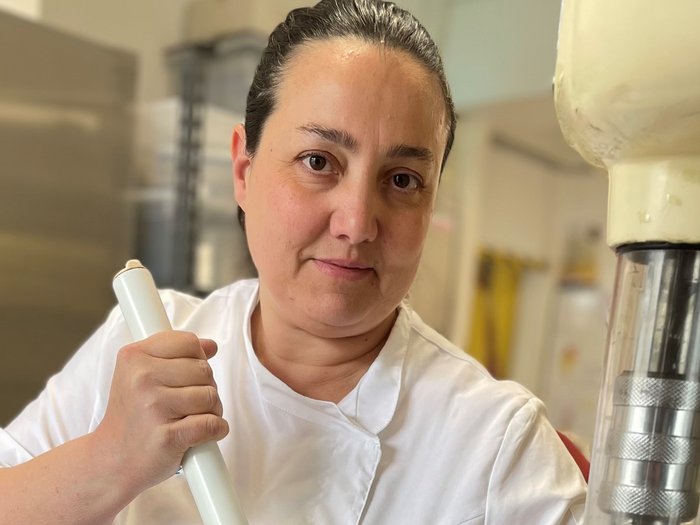 Mehr als nur eine Kugel Genuss: Warum handwerkliches Speiseeis die bessere Wahl ist Frau in weißer Kochjacke rührt mit großem Stab in Metallbehälter in Küche