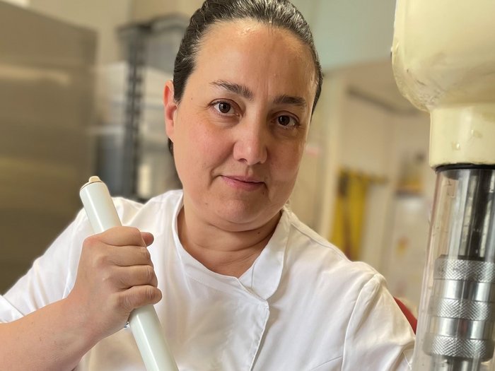Il gelato artigianale: semplicemente unico! Donna in giacca da cucina bianca mescola con bastone grande in contenitore metallico