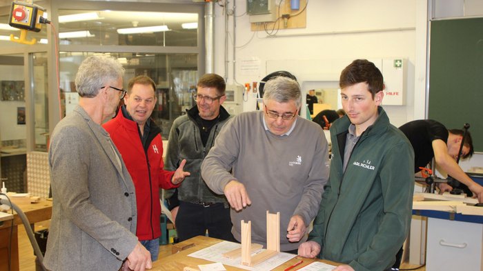 Jugendwettbewerb der Tischler/innen 2025: Südtirols Nachwuchstalente zeigen ihr Können Fünf Männer besprechen Holzprojekt in Werkstatt mit Zeichnungen und Modellen