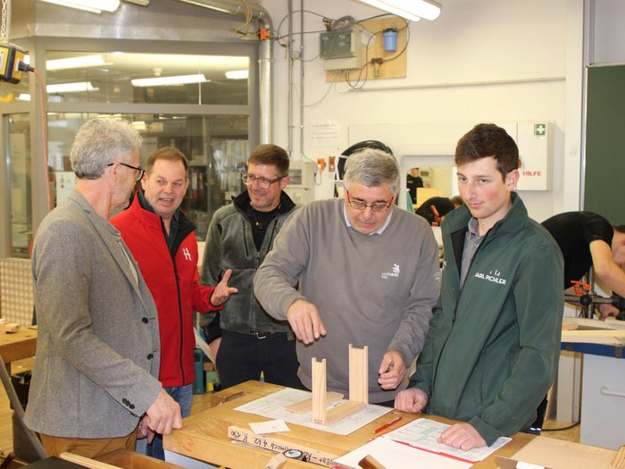 Jugendwettbewerb der Tischler/innen 2025: Südtirols Nachwuchstalente zeigen ihr Können Fünf Männer besprechen Holzprojekt in Werkstatt mit Zeichnungen und Modellen