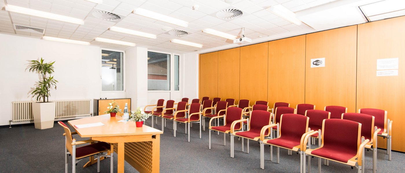 Affitto aule seminari Sala conferenze vuota con sedie rosse, tavolo di legno e finestre