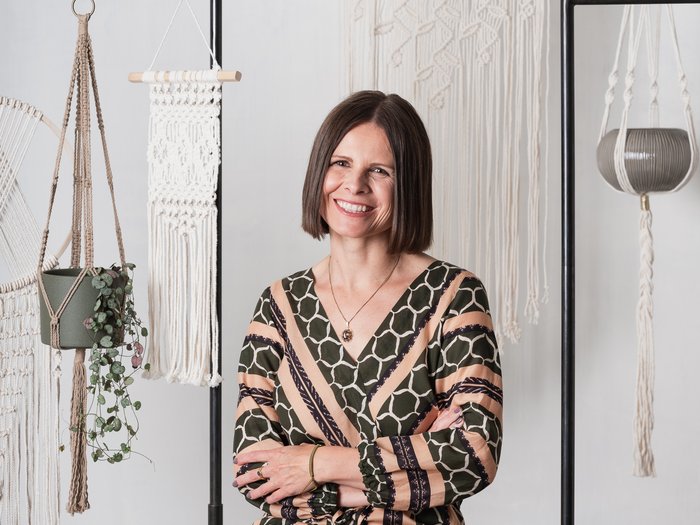 Workshop di “Punch Needle” alla VHS Südtirol: la creatività si unisce alla tradizione Donna seduta sorridente davanti a decorazioni da parete e portavasi in macramè