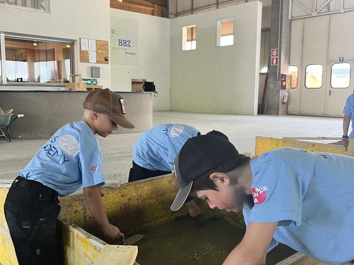 Kids Academy 2024: a Brunico l’artigianato colora l’estate dei più piccoli Bambini imparano in un capannone con casse di legno e attrezzi