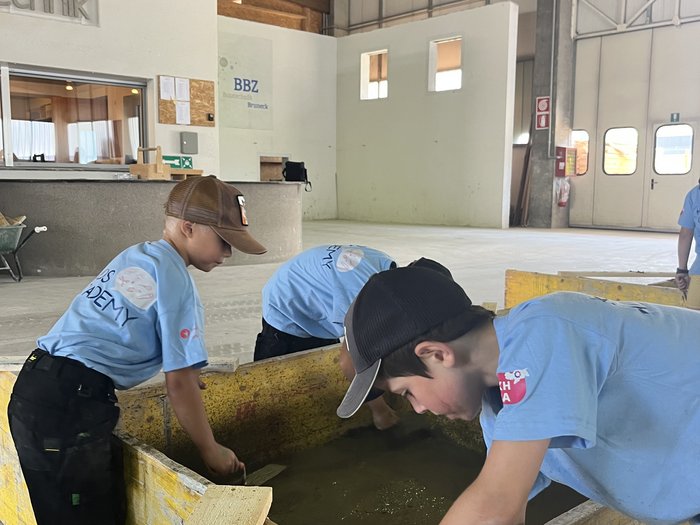 Kids-Academy 2024: buntes Handwerk in Bruneck Kinder lernen in einer Halle mit Holzboxen und Werkzeugen