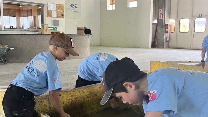 Kids-Academy 2024: buntes Handwerk in Bruneck Kinder lernen in einer Halle mit Holzboxen und Werkzeugen