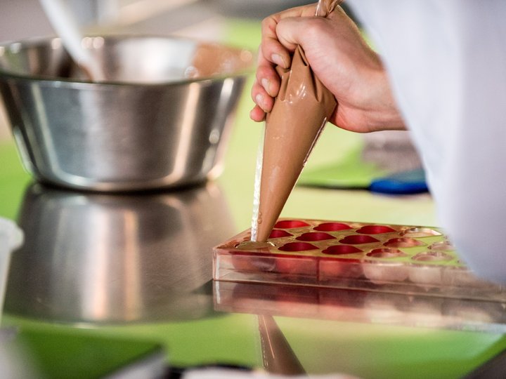 Ausbildung Hand füllt Schokoladenform mit Schokoladencreme aus Spritztüte