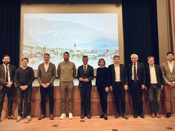 © Marktgemeinde Lana Gruppenfoto von zehn Personen auf Bühne vor Klimasymposium-Projektorbild