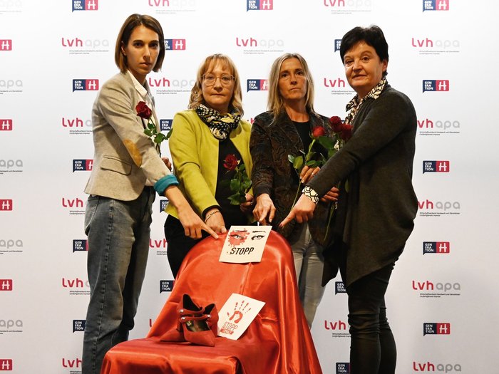 lvh setzt Zeichen gegen Gewalt an Frauen: ein „Besetzter Platz“ Vier Frauen mit Rosen zeigen auf rot bedeckten Stuhl mit Stoppschildern