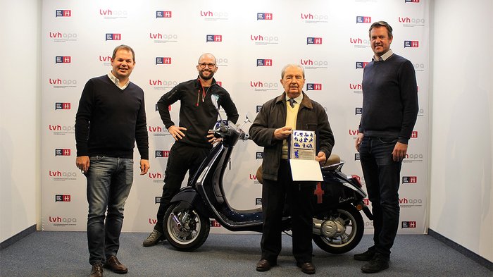Importante riconoscimento nazionale per l’artigiano Claudio Molinari Quattro uomini davanti a uno scooter e un premio in una stanza con logo LVH