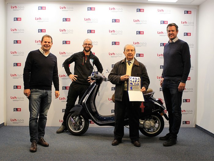 Importante riconoscimento nazionale per l’artigiano Claudio Molinari Quattro uomini davanti a uno scooter e un premio in una stanza con logo LVH