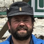 Untervinschgau Porträt eines bärtigen Mannes mit Brille und Mütze vor Steinmauer