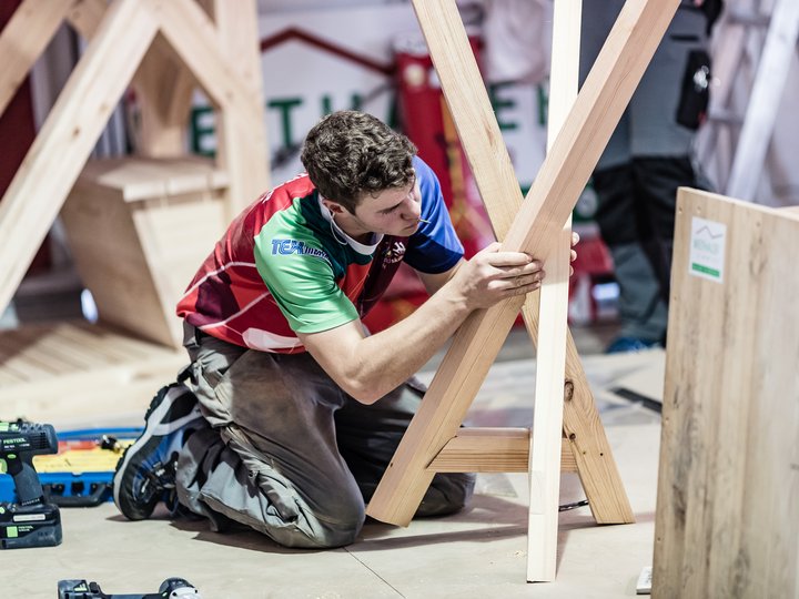 Costruttori in legno e carpentieri Uomo inginocchiato che lavora a struttura in legno con attrezzi a terra