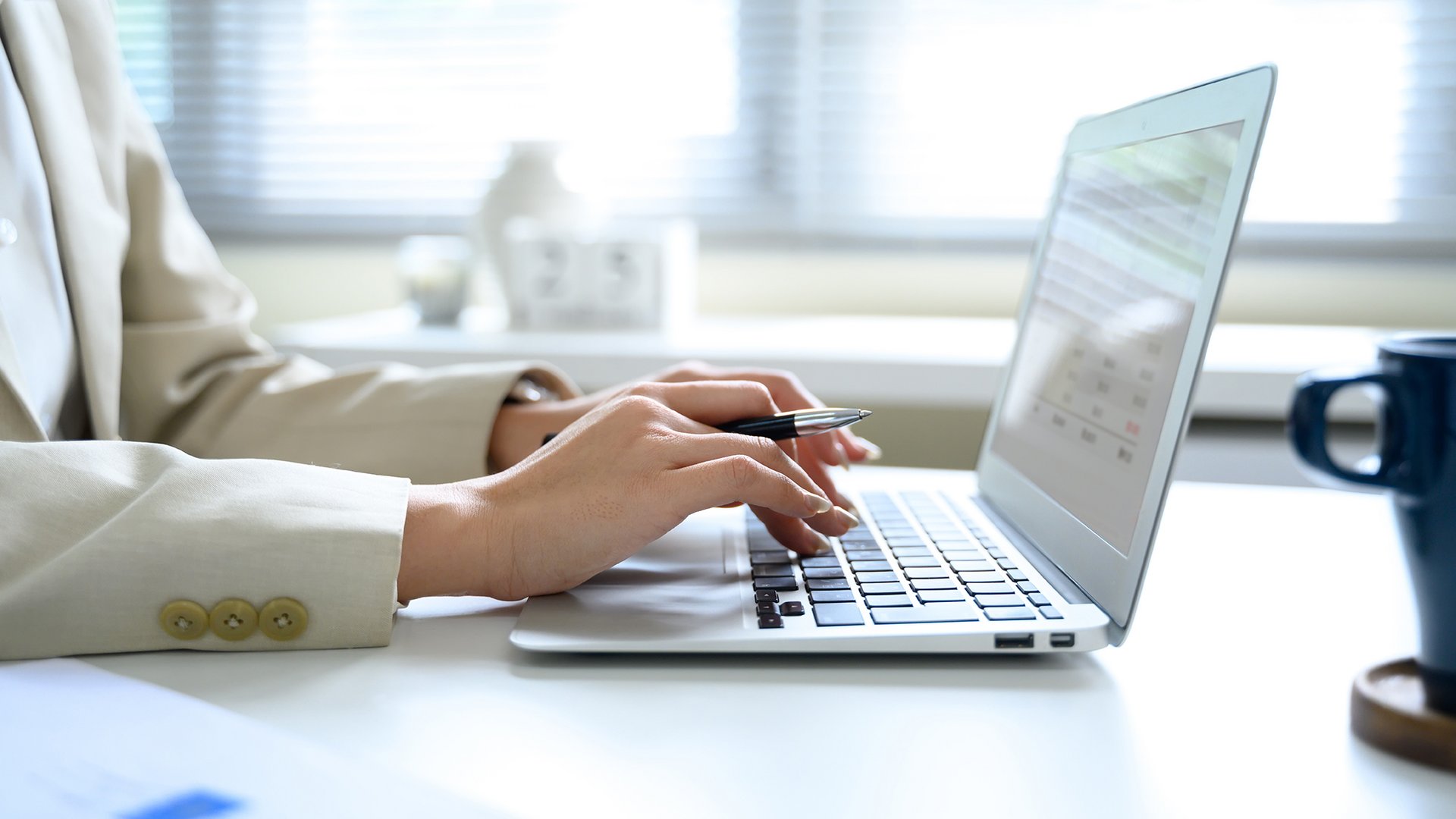 Home Persona digita sulla tastiera del laptop tenendo una penna in mano alla scrivania bianca