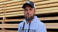 Der Südtiroler Zimmerer-Meistertitel wird jetzt in Deutschland anerkannt Mann mit Baseballkappe und weißem Hoodie hält Dokument vor Holzstapel