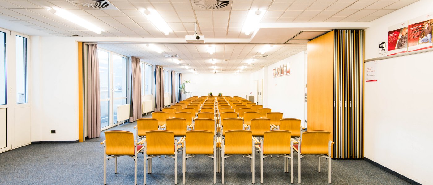 Affitto aule seminari Sala conferenze vuota con file di sedie in legno e grandi finestre