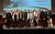 Foto di gruppo di 17 persone su un palco davanti a uno schermo di presentazione