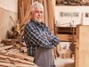 Home Artigiano anziano con grembiule in una falegnameria con plance di legno