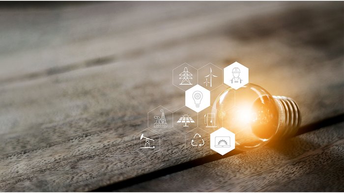 Via al primo percorso formativo altoatesino in tema di sostenibilità Lampadina con simboli di energia e sostenibilità su tavolo di legno