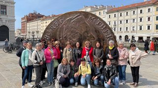 News Gruppe von Frauen vor großer Münzenskulptur auf einem Platz in der Stadt