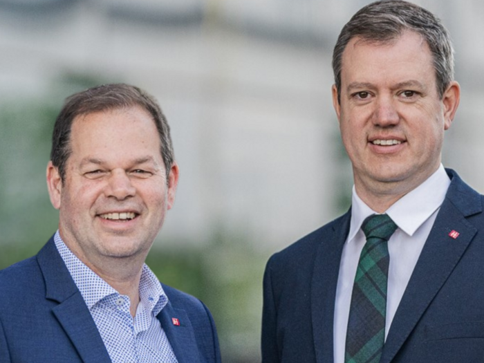 Digitalisierungsoffensive: wertvolles Instrument Zwei Männer in Anzügen lächeln vor einem unscharfen Hintergrund