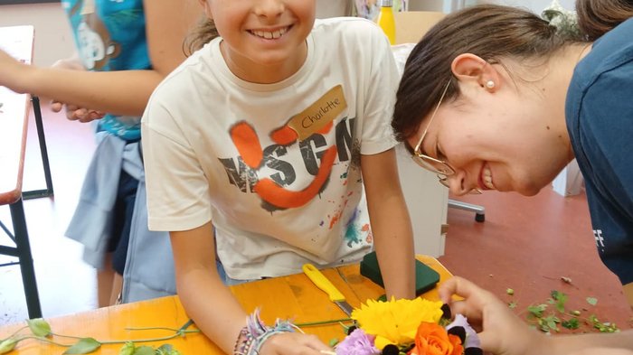 KidsAcademy 2025: Ein Sommer voller Handwerk und Kreativität Mädchen arrangiert bunte Blumen auf Tisch im Floristik-Workshop