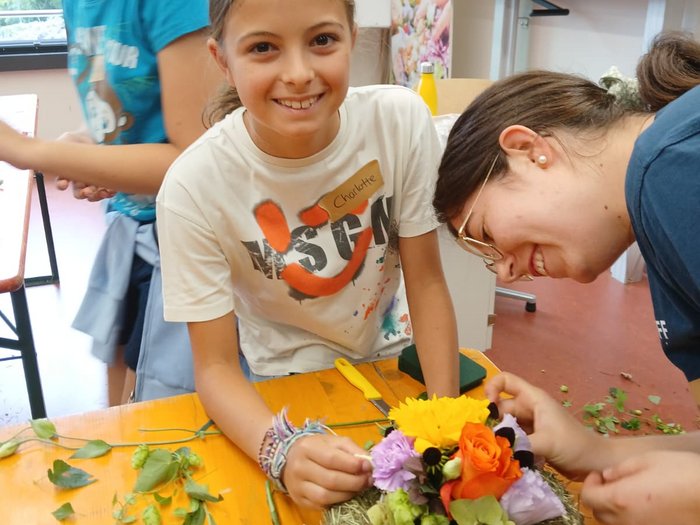 KidsAcademy 2025: Ein Sommer voller Handwerk und Kreativität Mädchen arrangiert bunte Blumen auf Tisch im Floristik-Workshop