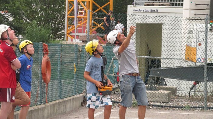 Kinder und Jugendliche lernen die Welt der Baumaschinen Gruppe von Personen mit Helmen beobachtet etwas über ihnen auf einer Baustelle