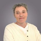 Astrid Treibenreif Ritratto di donna anziana con capelli corti grigi e maglione bianco su sfondo grigio