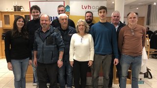 News Gruppenfoto von elf Personen in einem Raum mit Werbebannern im Hintergrund