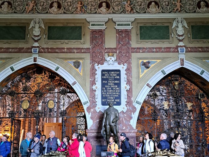 Reisefreudige Althandwerker/innen Innenansicht von Schloss mit Statue, reich verzierten Sarkophagen und Besuchergruppe