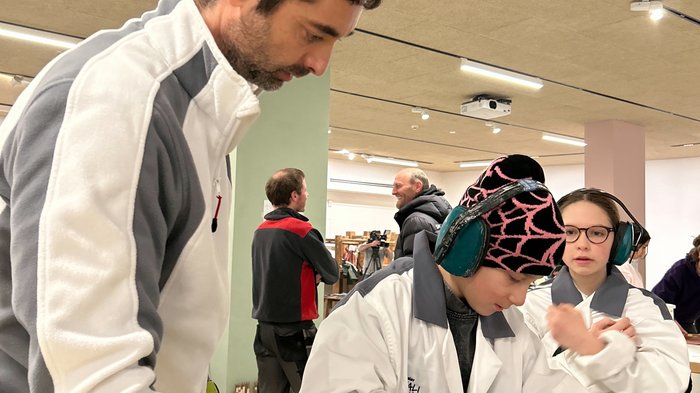 Vivere da vicino l'esperienza dell'artigianato: i mestieri pratici incontrano il futuro in Val Gardena Adulto supervisiona bambino che utilizza levigatrice in officina