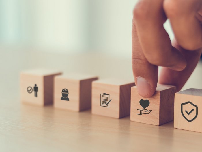 Neuer territorialer Gesundheitsfonds für das Baugewerbe Hand berührt Holzklotz mit Herzsymbol unter anderen Symbolen
