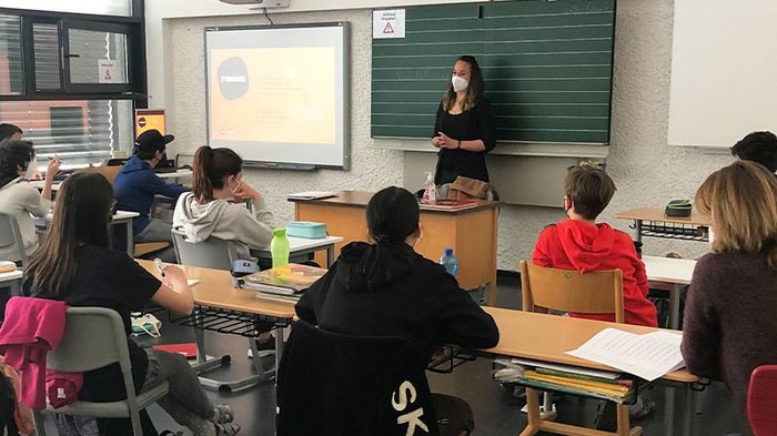 In die Welt der praktischen Berufe eintauchen Lehrerin mit Maske unterrichtet Schüler im Klassenzimmer mit Beamer