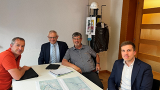 News Vier Männer in einem Büro sitzen am Tisch mit Karten und Notizen