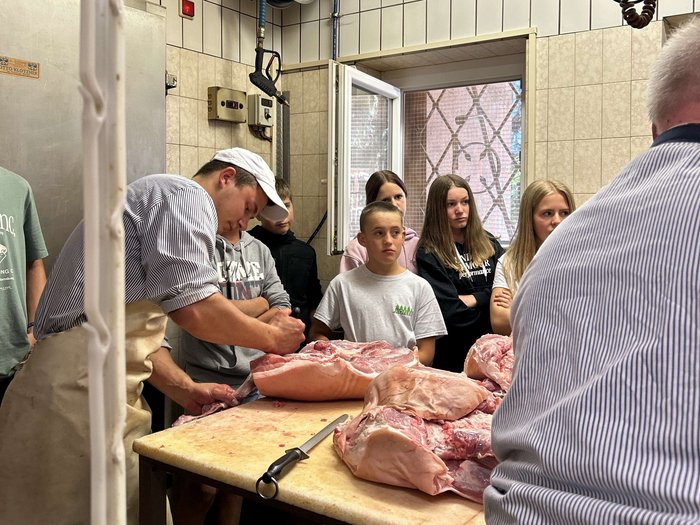 Praxis statt Theorie: Schulbesuche bei Handwerksbetrieben in St. Leonhard Menschen beobachten Fleischer bei der Fleischzerlegung auf einem Tisch