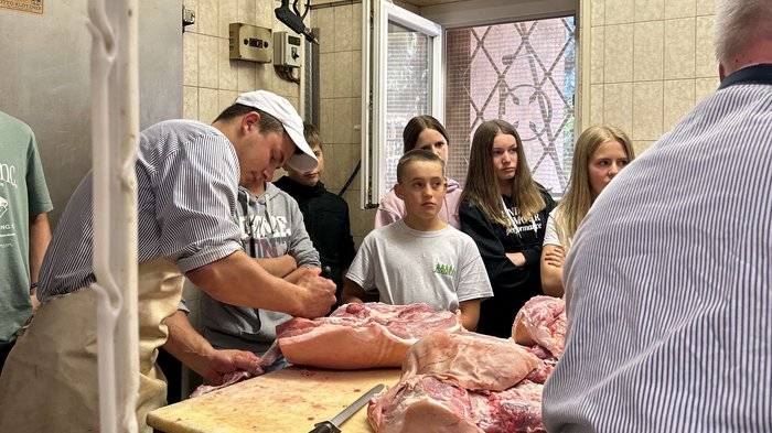 Praxis statt Theorie: Schulbesuche bei Handwerksbetrieben in St. Leonhard Menschen beobachten Fleischer bei der Fleischzerlegung auf einem Tisch