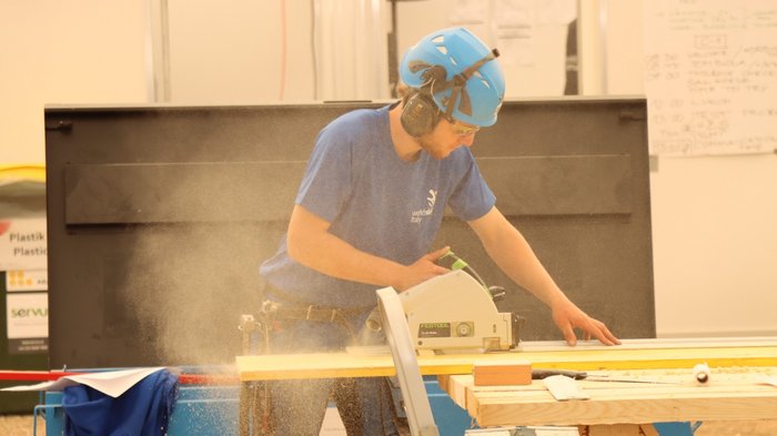 EuroSkills 2021 Mann mit Helm und Schutzbrille sägt Holz mit Kreissäge auf einer Werkbank