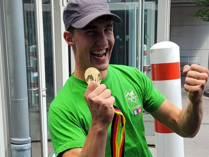 Foto 1 - Marcel Bolego © Südtiroler Zimmerer Junger Mann freut sich mit Medaille und grünem T-Shirt im Freien
