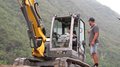 Kinder und Jugendliche lernen die Welt der Baumaschinen Kind lernt Baggerfahren mit Erwachsenem im Freien vor bewaldetem Hügel
