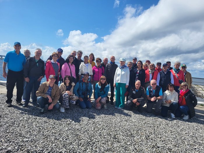 Reisefreudige Althandwerker/innen Gruppe von Erwachsenen am Strand mit blauem Himmel und Wolken