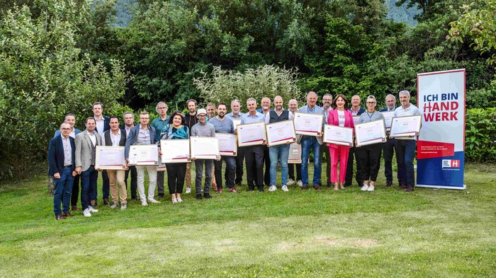 Consegna della spilla d’oro di lvh.apa Foto di gruppo di persone con certificati davanti a un banner Ich bin Handwerk all'aperto