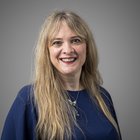 Daniela Sbironi Ritratto di donna sorridente con capelli biondi lunghi e maglia blu su sfondo grigio