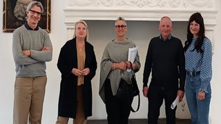 News Fünf Personen stehen vor einem dekorativen weißen Kamin mit Gemälde an der Wand