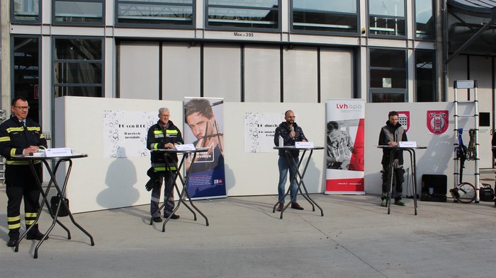 Kohlenmonoxid: Information und Prävention Mehrere Männer stehen an Tischen vor einem Gebäude, einige in Feuerwehruniformen
