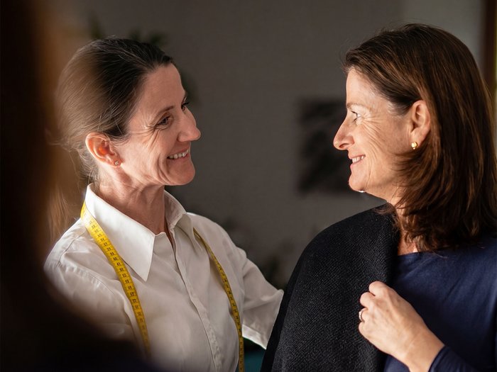 Maßarbeit im Aufbruch Zwei lächelnde Frauen beim Anpassen eines Kleidungsstücks im Atelier