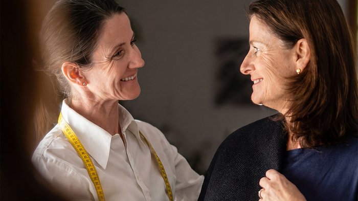 I test continuano ad essere necessari Due donne sorridenti che adattano un capo in un laboratorio di sartoria