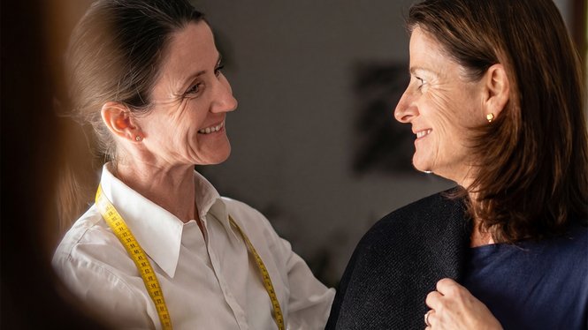 Home Zwei lächelnde Frauen beim Anpassen eines Kleidungsstücks im Atelier