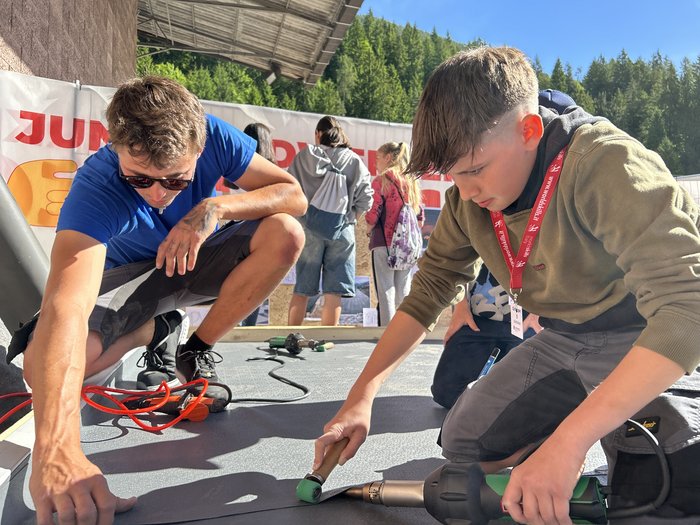 SkillsDay nella Val d'Ega: scoprire l'artigianato, scoprire talenti Ragazzo impara mestiere con pistola termica e rullo all'aperto sotto supervisione
