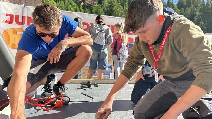 SkillsDay nella Val d'Ega: scoprire l'artigianato, scoprire talenti Ragazzo impara mestiere con pistola termica e rullo all'aperto sotto supervisione