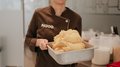 "Gambero Rosso": premiata la gelateria AiJOO Donna in uniforme marrone tiene un contenitore con gelato appena fatto